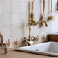 A tiled splashback behind a farmhouse kitchen sink made up of plain cream marble tiles, with a row of tiles featuring a watercolour pheasant design.