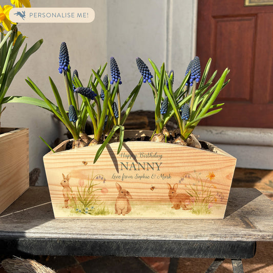 An arched wooden planter planter box showing a watercolour design of bunny rabbits among pastel spring flowers. The planter can be personalised with names and a selection of phrases to suit any occasion, including wedding, anniversary, engagement, birthday and new home.
