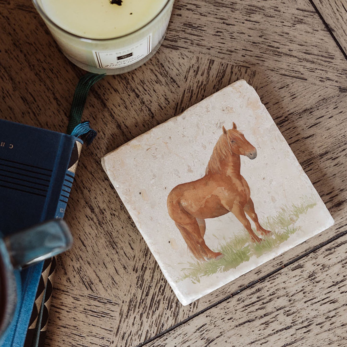 A square marble coaster on a bedside table, featuring a watercolour design featuring a watercolour design of a rare breed Suffolk Punch horse in a grassy field.