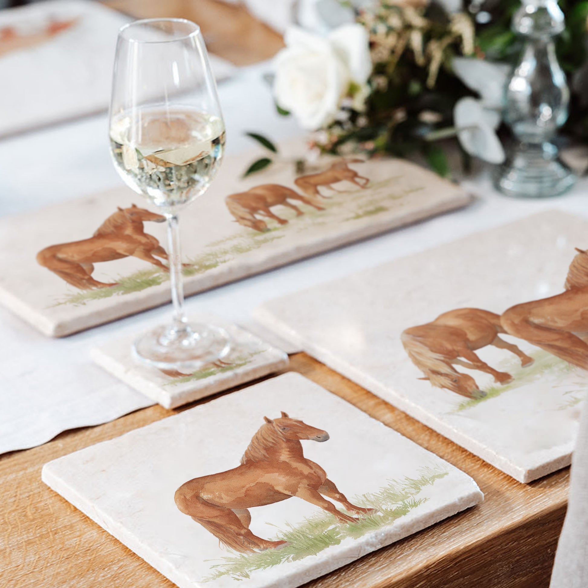 A wooden dining table set with cream marble placemats and coasters. The placemats are square and feature some stunning Suffolk punch horses in a watercolour style.