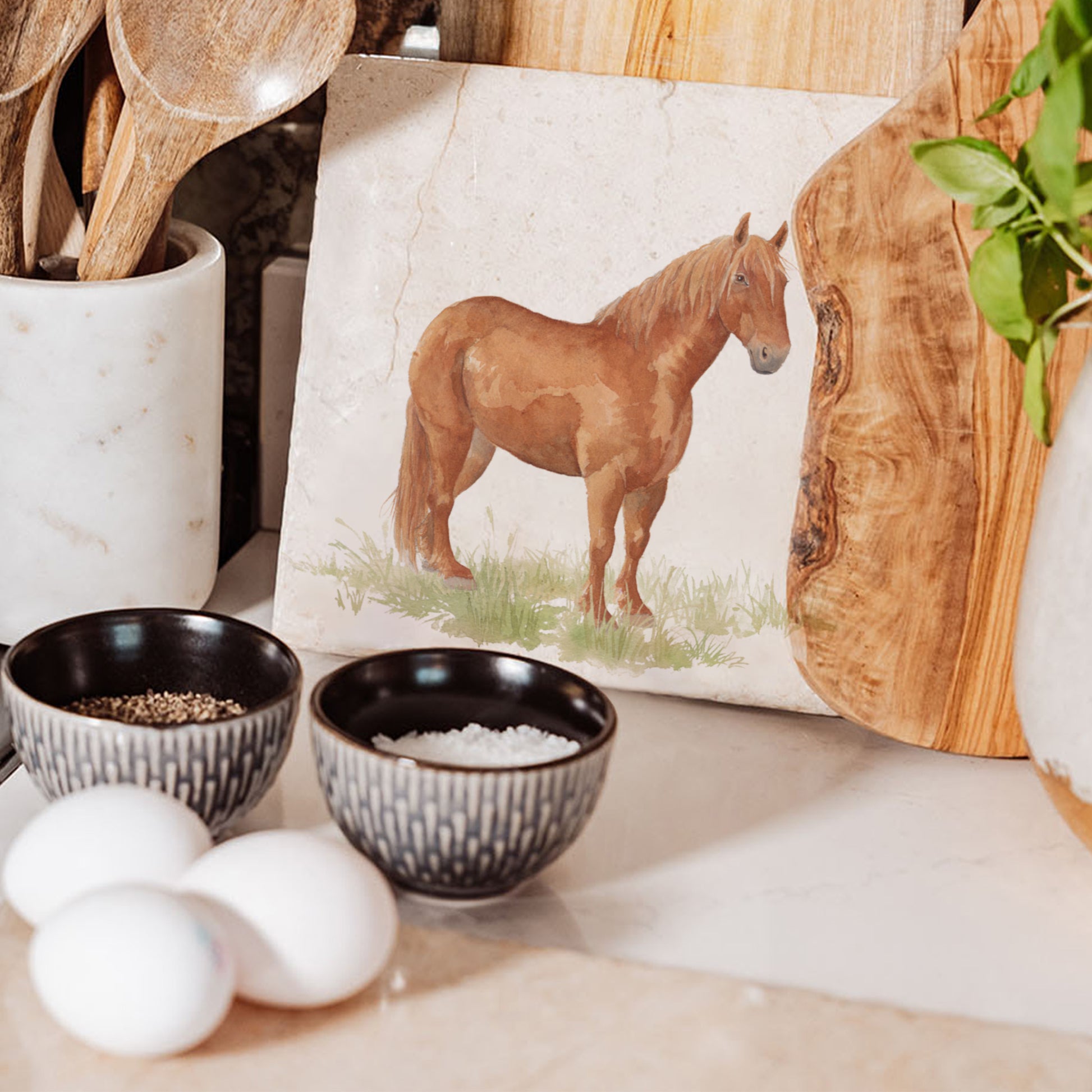 A medium square multipurpose marble chopping board propped up on a country kitchen worksurface, featuring a watercolour design of a rare breed Suffolk Punch horse in a grassy field.
