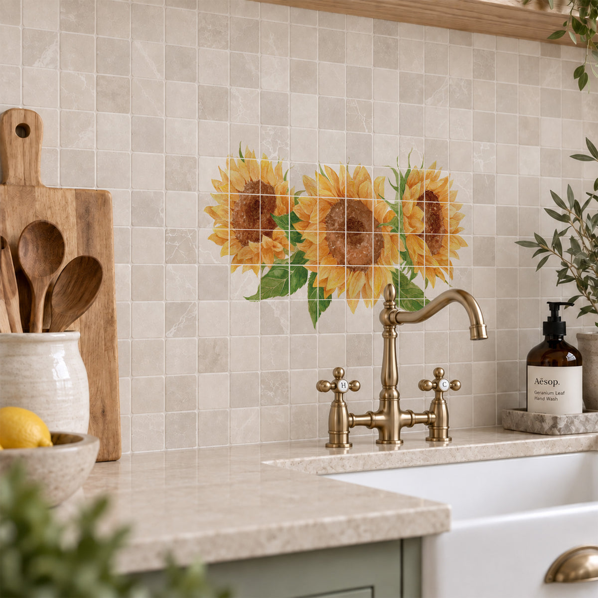 A set of square mosaic tiles featuring a decorative sunflower design, installed on a kitchen backsplash above a brass faucet and white farmhouse sink.
