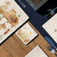 A marble coaster set on a dining table. the coaster has a watercolour design of spring flowers and cute fluffy bunnies. 