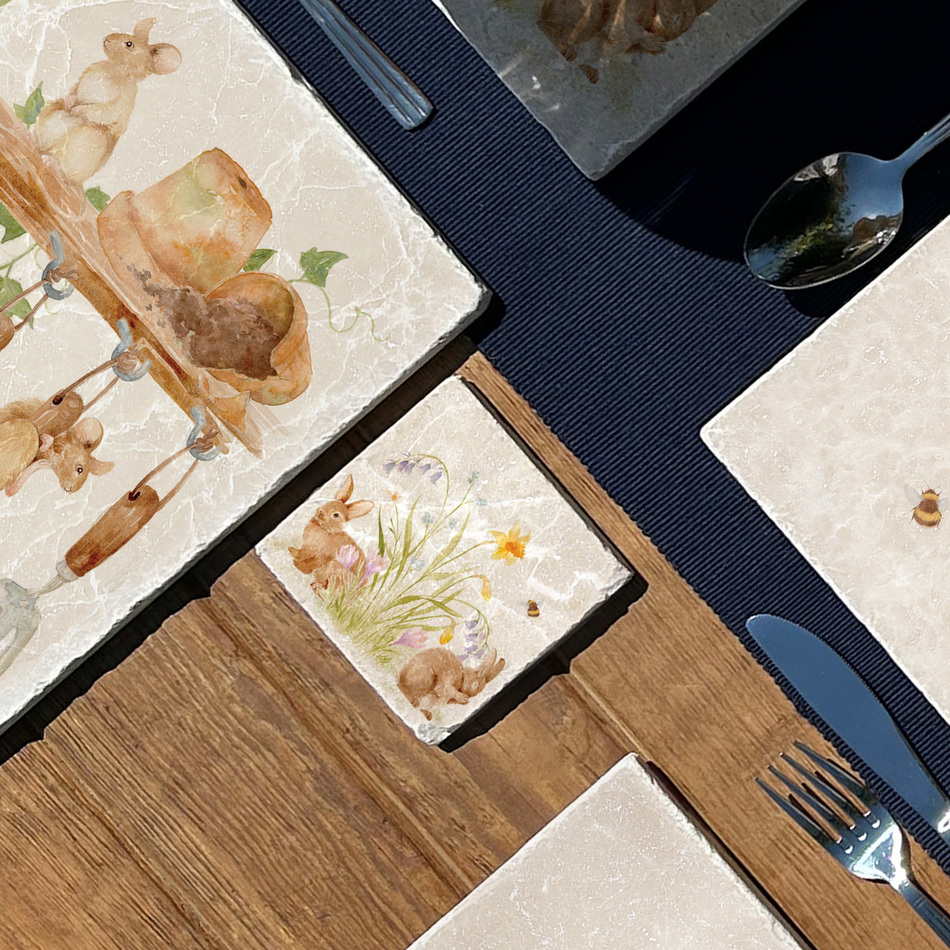 A marble coaster set on a dining table. the coaster has a watercolour design of spring flowers and cute fluffy bunnies. 