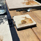 A marble coaster set on a dining table with placemats featuring a watercolour design of mischievous rabbits amongst the terracotta flowerpots and spring flowers.