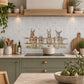 A kitchen backsplash made of light gray marble tiles with a decorative graphic of three cartoon donkeys in a wooden fence. The kitchen features sage green cabinets, a light wood range hood, and various cooking utensils and plants.