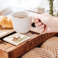 A woman's hand placing a coffee cup on a marble coaster. The coaster design features a red deer stag and hind.