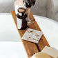 A square marble coaster on a wooden bath tidy above a bubble bath. The coaster features a British garden birds watercolour design.