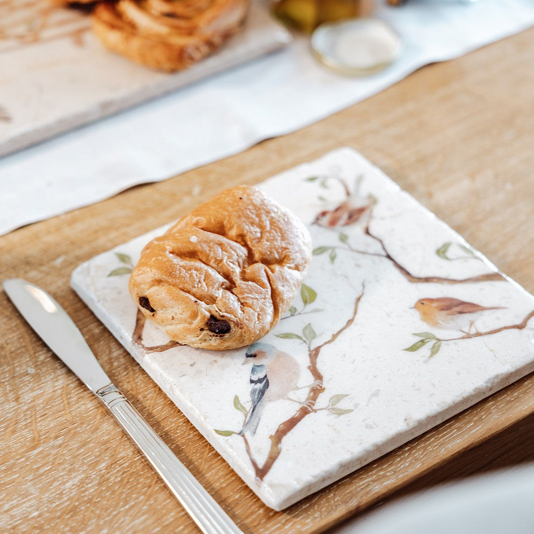 A medium multipurpose marble platter with a watercolour design featuring British garden birds on branches. The platter is being used as a plate for breakfast pastries.