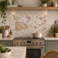 A decorative kitchen backsplash tile featuring a watercolour vintage-style illustration of birds perched on branches and a wooden fence, installed on a light grey tiled wall above a black stovetop in a styled kitchen setting.