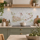 A decorative kitchen backsplash tile featuring a watercolour vintage-style illustration of birds perched on branches and a wooden fence, installed on a light grey tiled wall above a black stovetop in a styled kitchen setting.