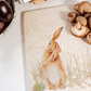 A large square marble platter on a kitchen worktop with a recipe book propped up behind it. The platter has a hare design on it, and is being used as a worktop saver.