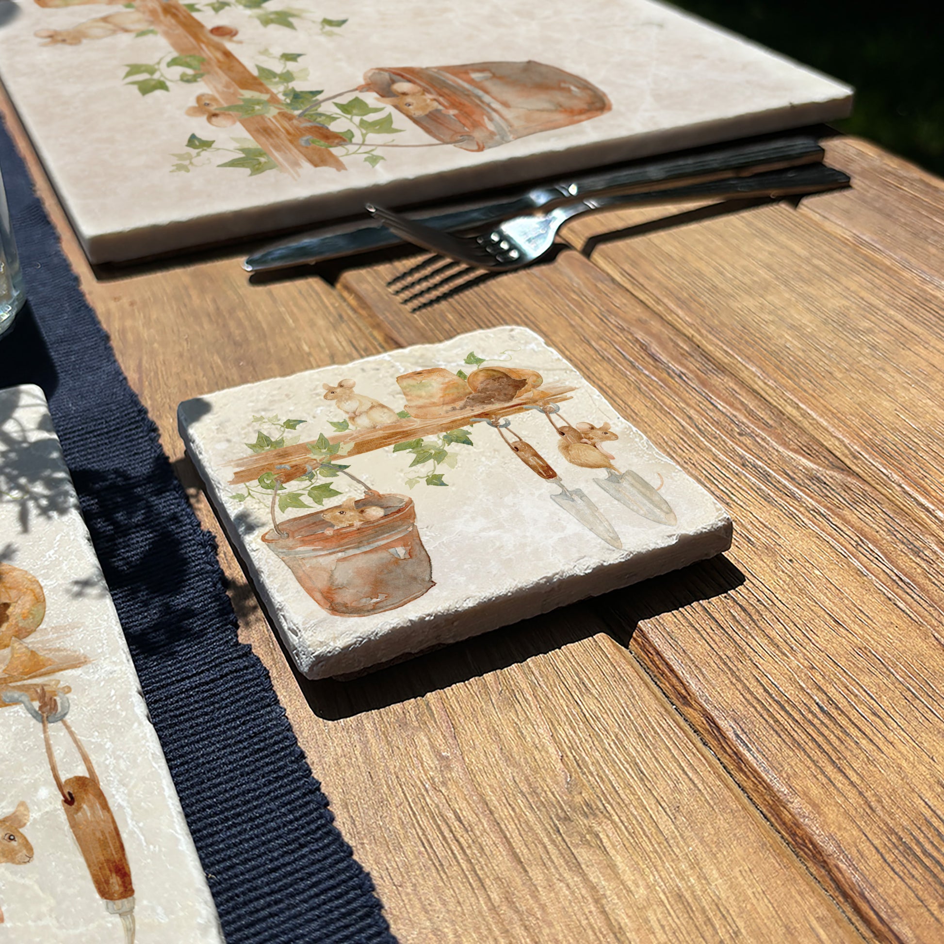 A marble coaster featuring a  watercolour design of mice in a garden shed among the flowerpots and tools.
