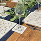 A square marble coaster with a watercolour pattern of busy bees and purple lavender flowers. The coaster is set on an outdoor table with matching placemats.