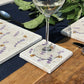 A handmade marble coaster featuring a watercolour pattern of busy bees and lavender flowers. The coaster is set on a garden dining table.