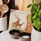 A medium marble personalised cheese board propped up on a kitchen worktop. The cheese board features a red deer stag and hind in a watercolour style.