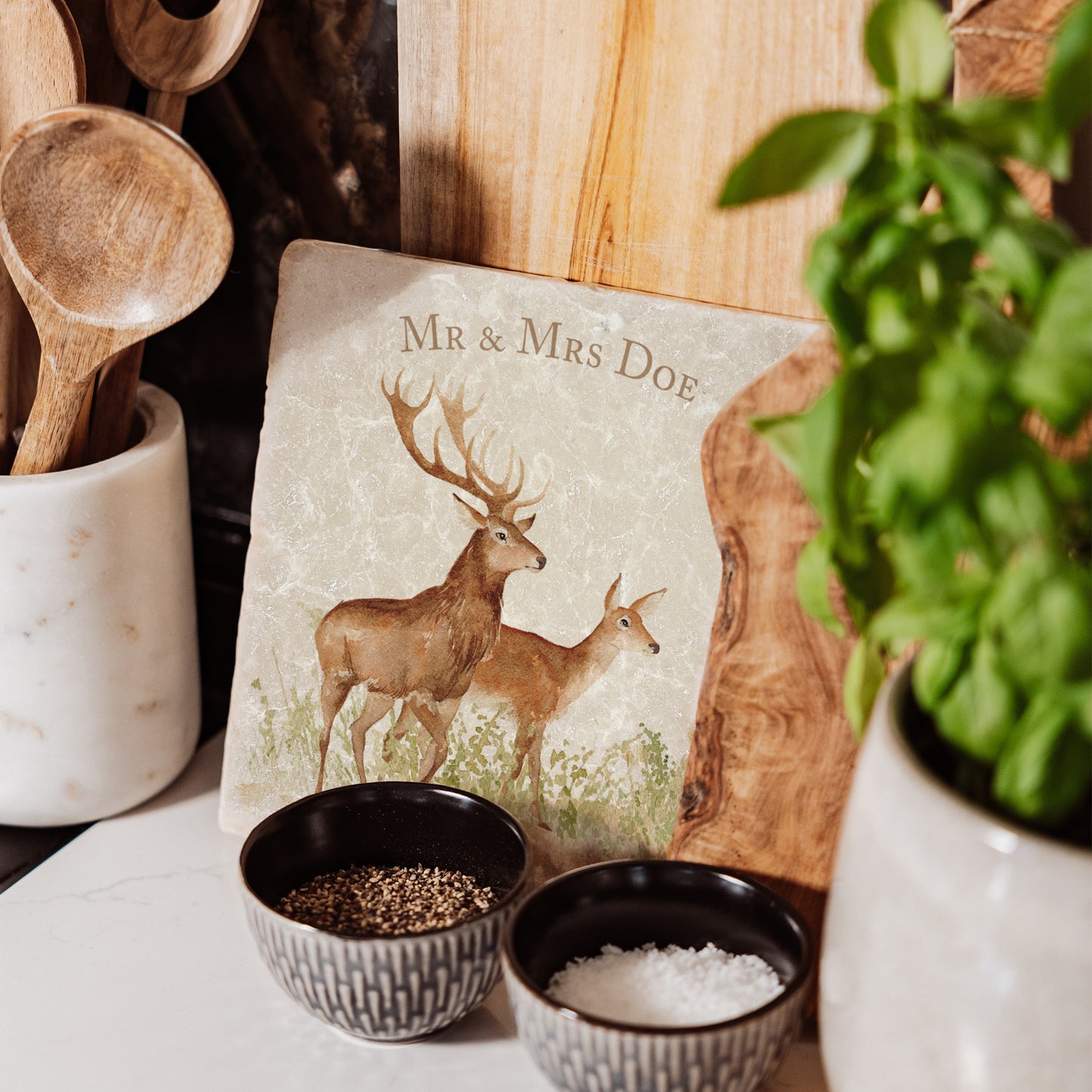 A medium marble personalised cheese board propped up on a kitchen worktop. The cheese board features a red deer stag and hind in a watercolour style.