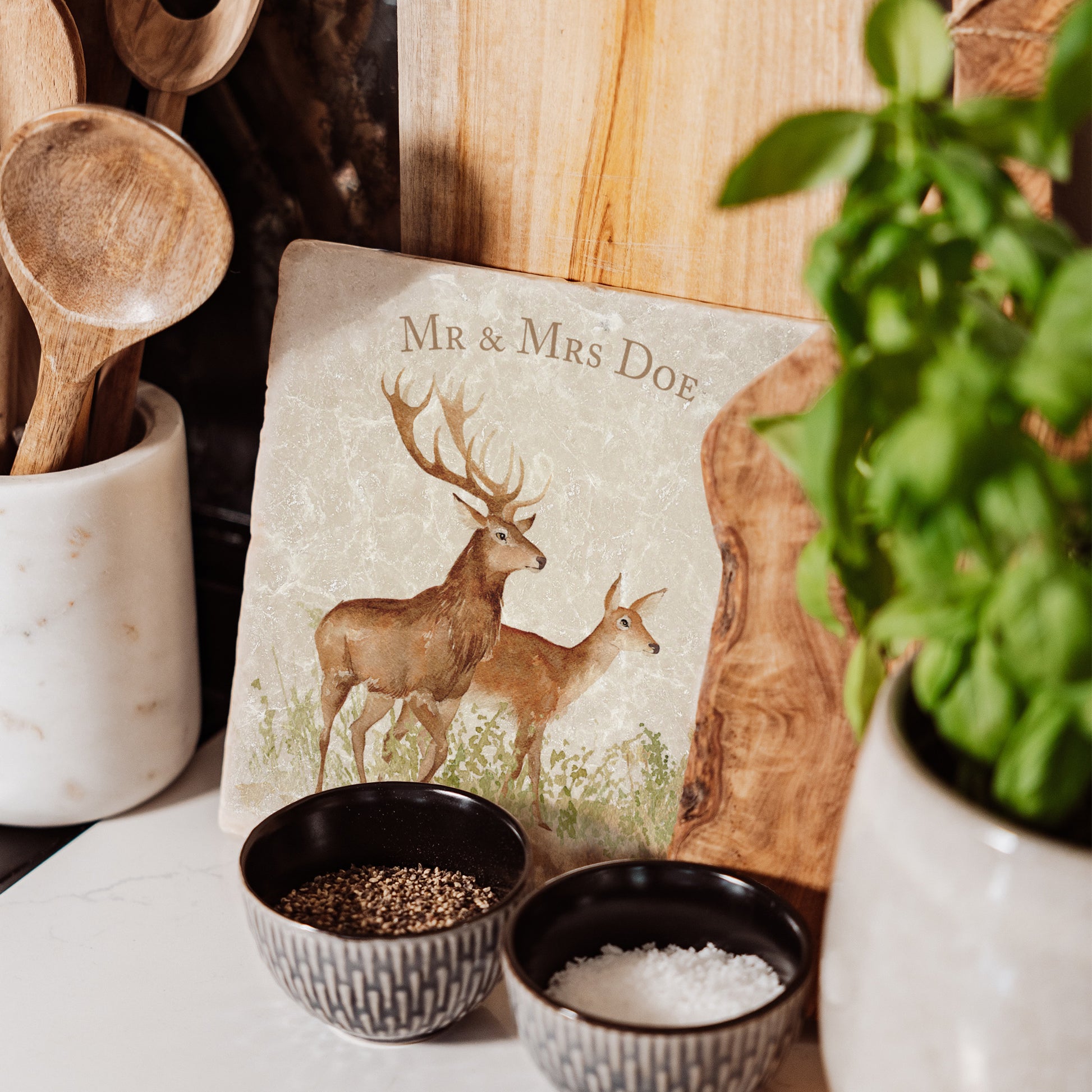 A medium marble personalised cheese board propped up on a kitchen worktop. The cheese board features a red deer stag and hind in a watercolour style.
