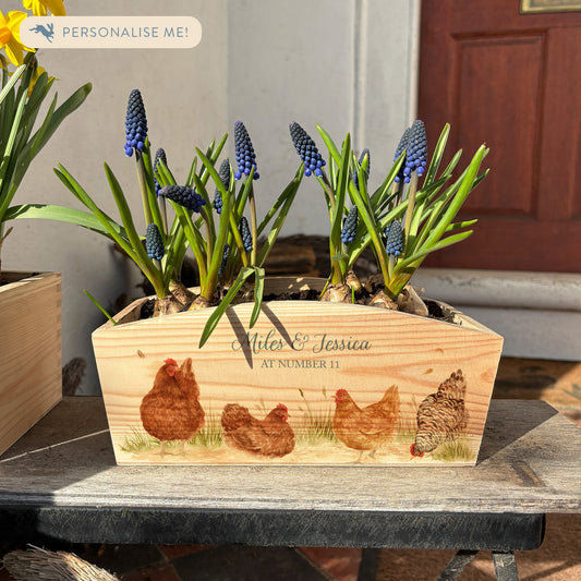 An arched wooden planter box full of spring bulbs. The planter box shows a watercolour design of a flock of hens pecking in the farmyard. The planter can be personalised with names and a selection of phrases, making it an ideal gift for any occasion.