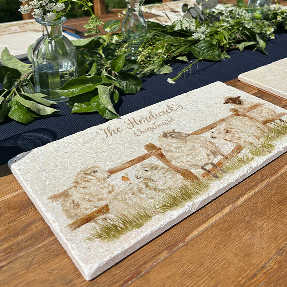 A personalised marble sharing platter featuring a herd of sheep set on a garden table as a centrepiece for serving dishes. The bespoke text displays the famaily name.