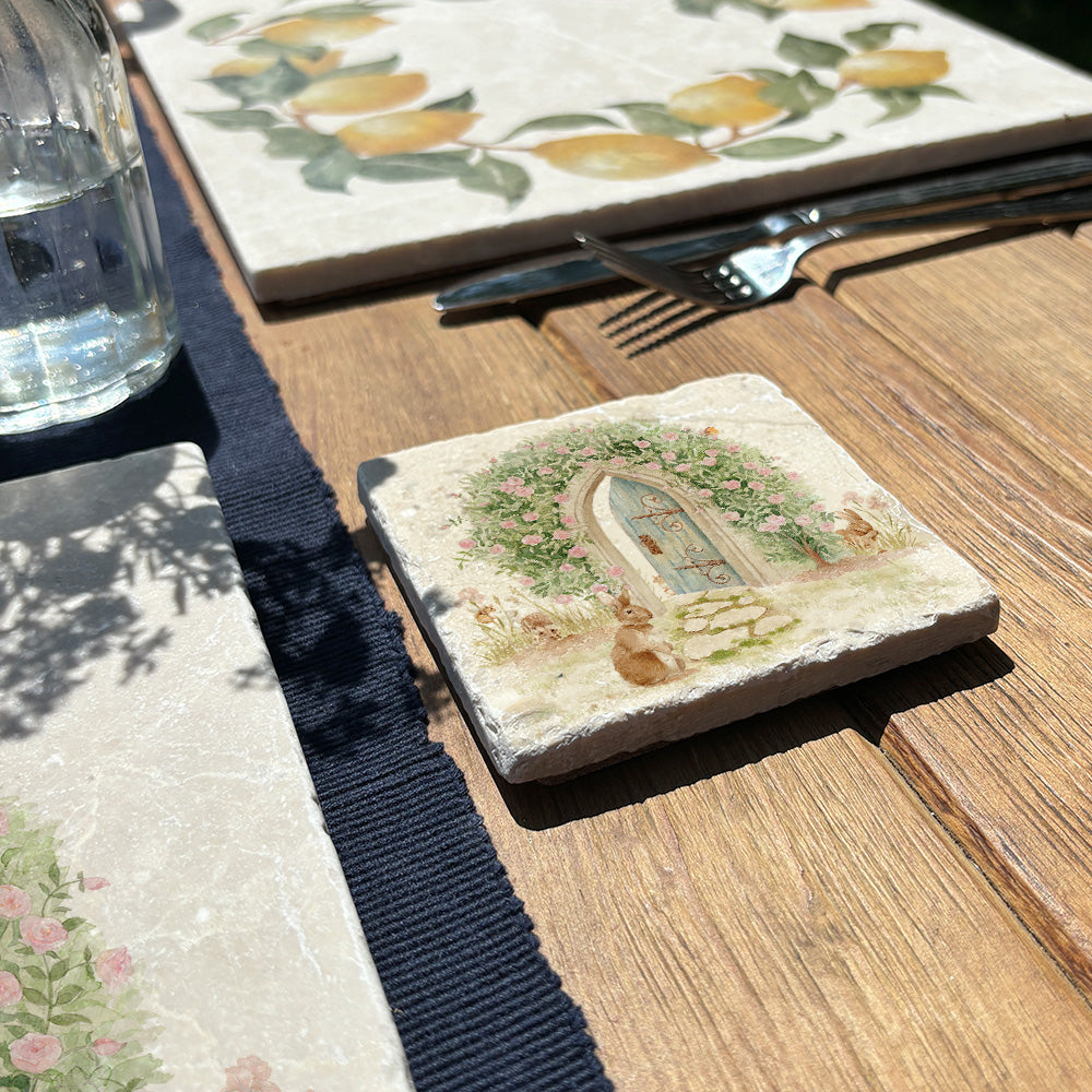 A square marble coaster featuring a  watercolour design of a hidden door under a rose archway and leading into an enchanted garden.