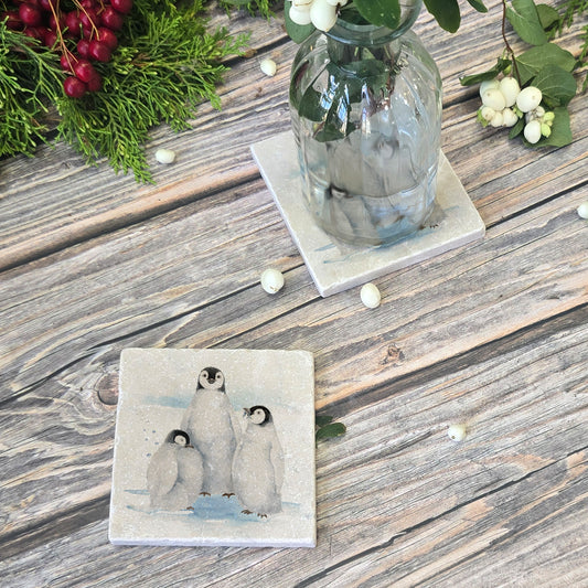 Coaster with penguin design on a wooden surface with a vase and greenery.