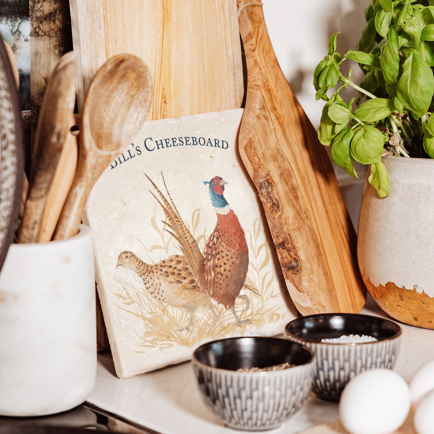 A medium personalised square marble chopping board, featuring a watercolour design of a pair of pheasants, one male and one female, in golden grass.
