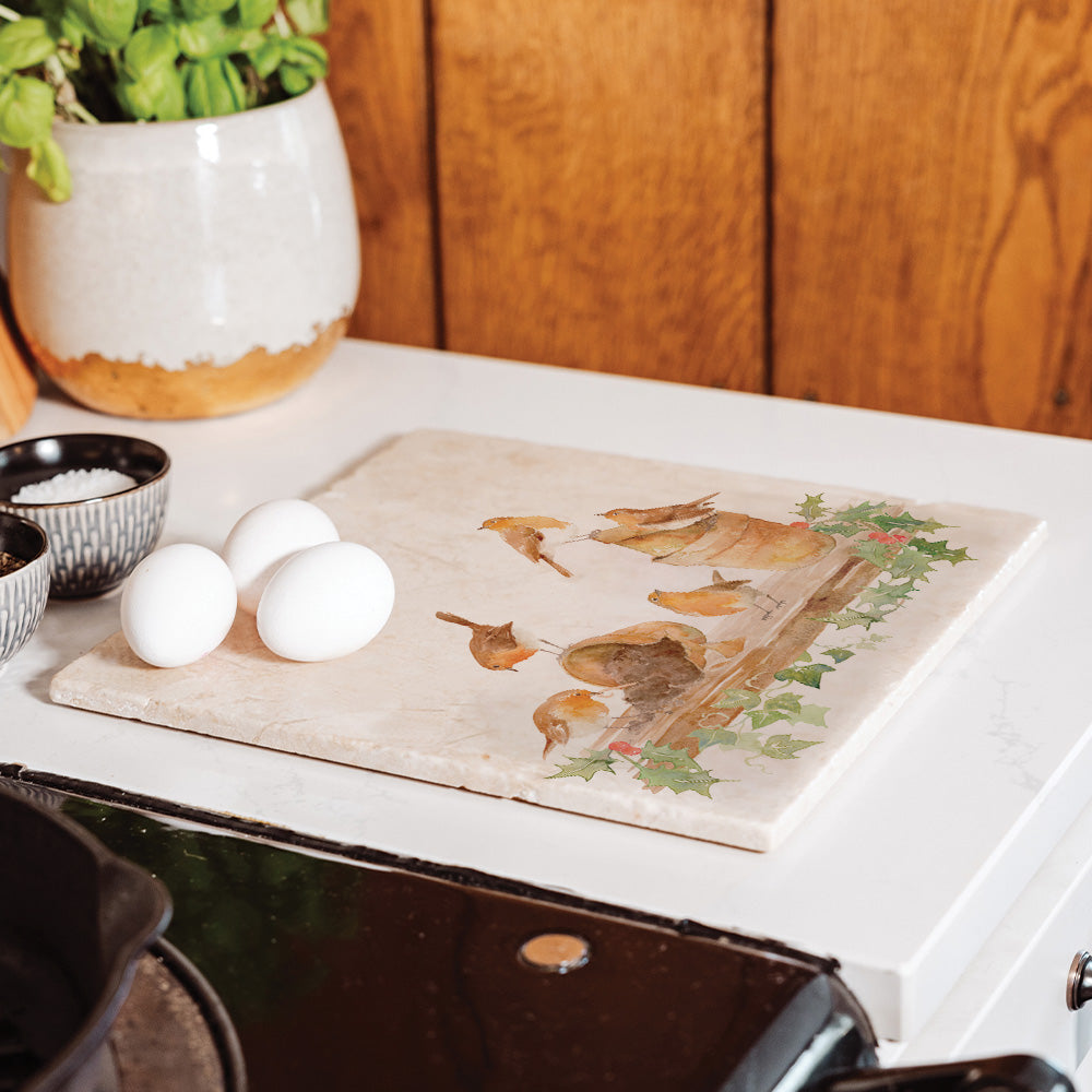 A large marble worktop saver with a Christmas robin and holly design, set on the side next to the hob.