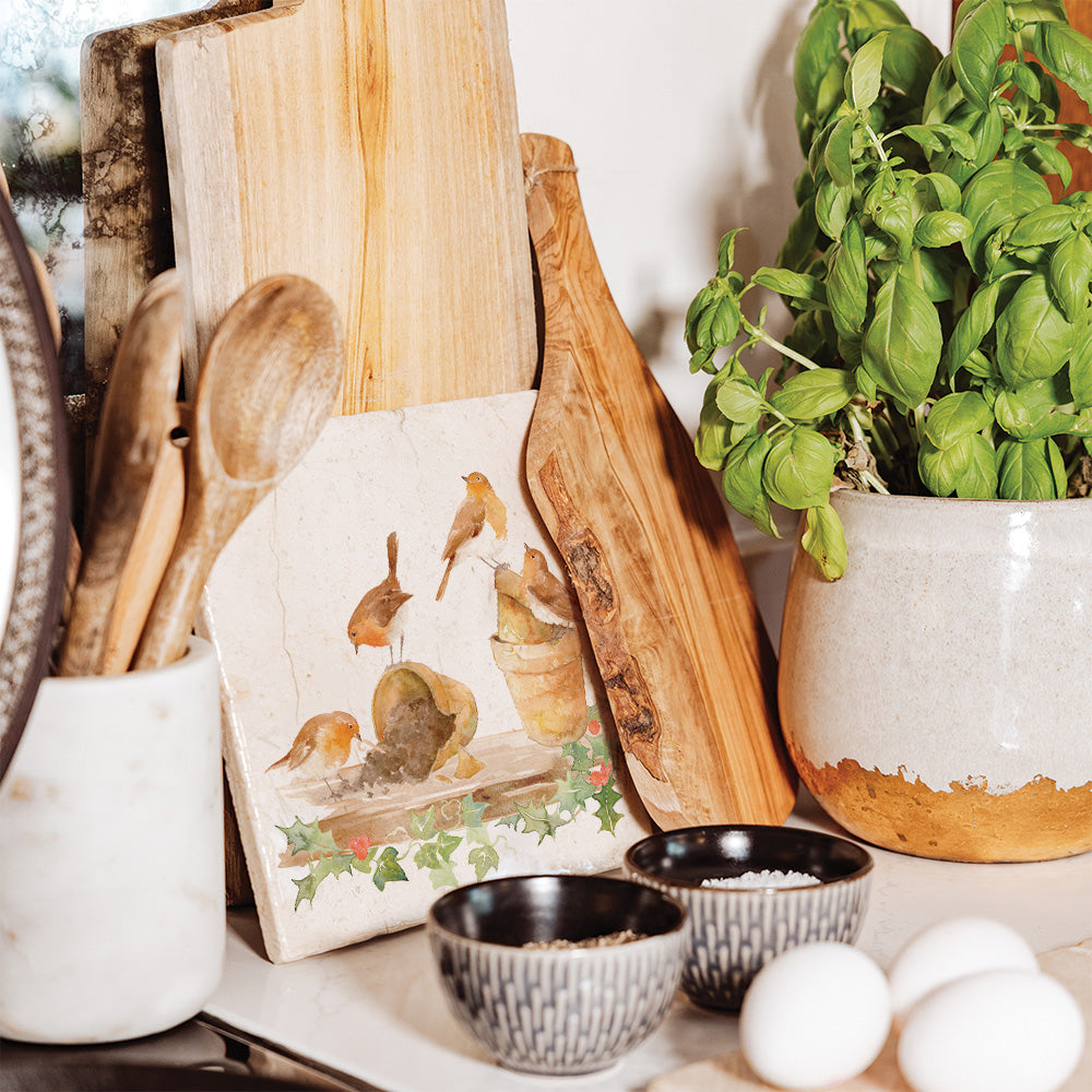 A hand made medium marble trivet propped up on a worksurface. The trivet has a Christmas design featuring robins and holly.