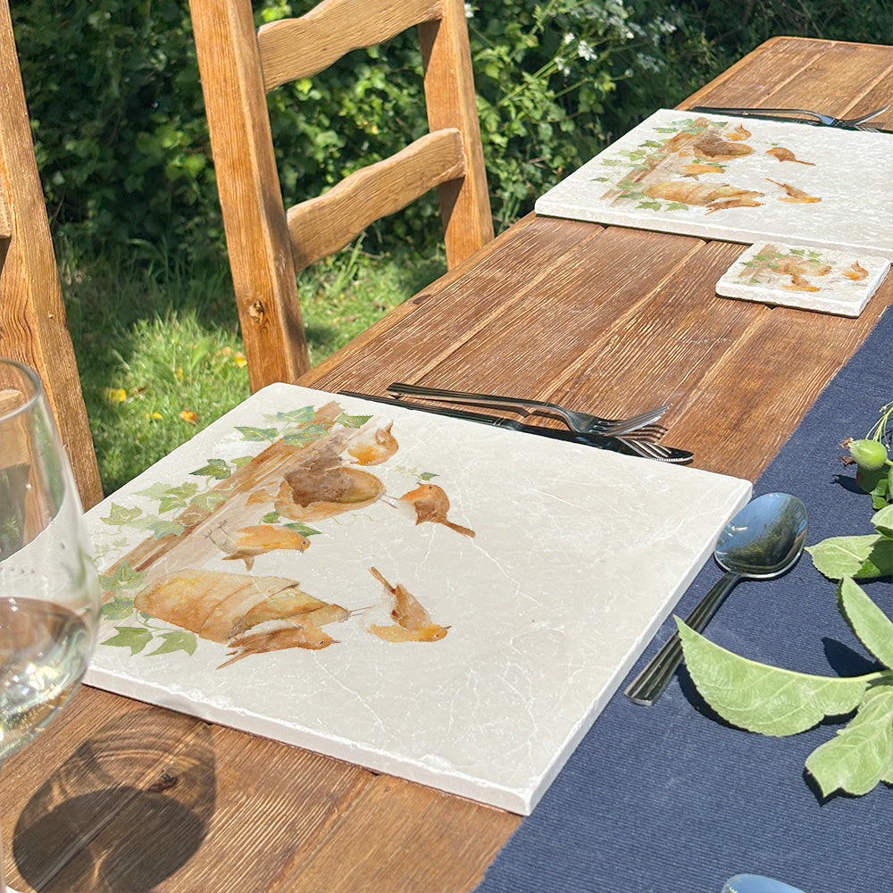 A garden table set with large cream marble placemats that feature a rabble of robins causing trouble in the potting shed. 