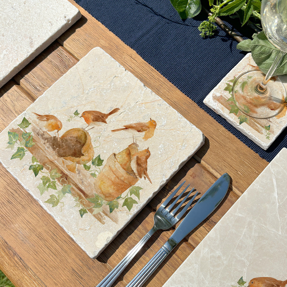 An outdoor table set with marble platters to serve from. The medium marble platter has a watercolour design showing a rabble of robins creating trouble in the potting shed.