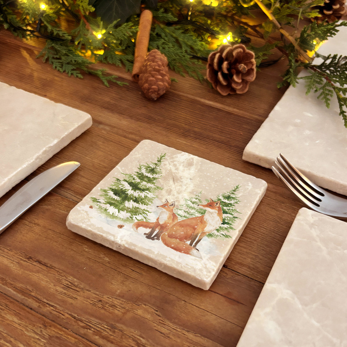 Set of four square marble coasters featuring a winter forest illustration with a fox family and evergreen trees in the snow.