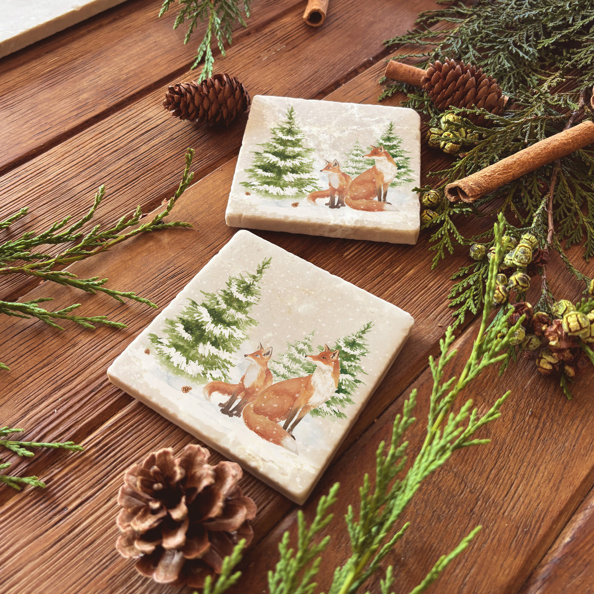 Set of four square marble coasters featuring a winter forest illustration with a fox family and evergreen trees in the snow.
