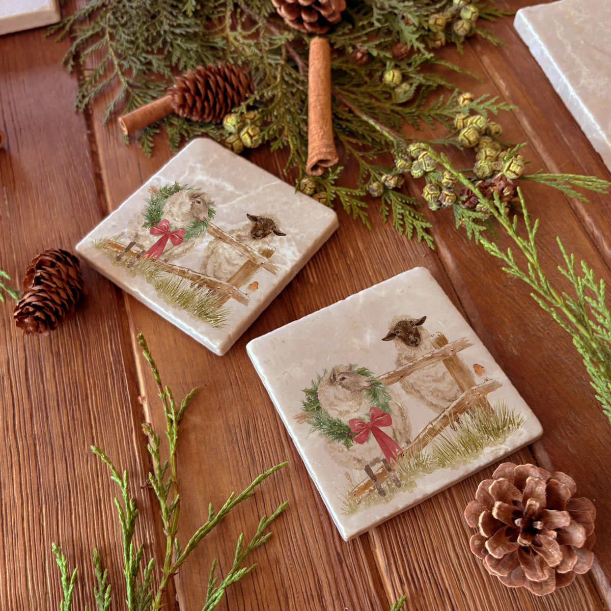 A set of four square marble coasters with a watercolour illustration of a farmyard scene, with sheep in the snow wearing a Christmas wreath.
