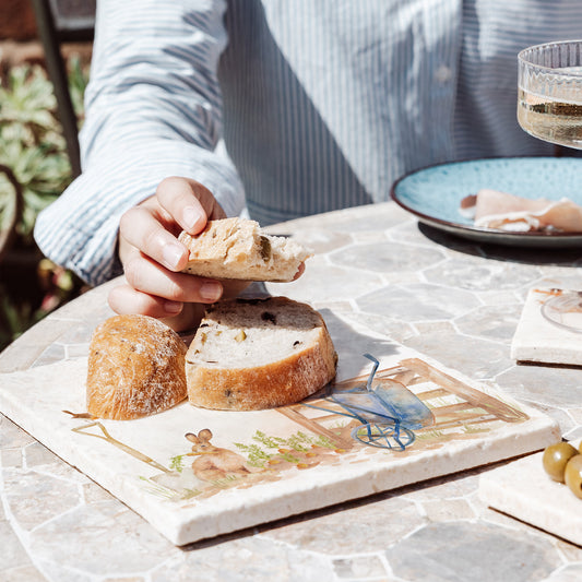 A medium cream marble platter on a garden table, being used to serve bread. The platter has a watercolour vegetable patch design.