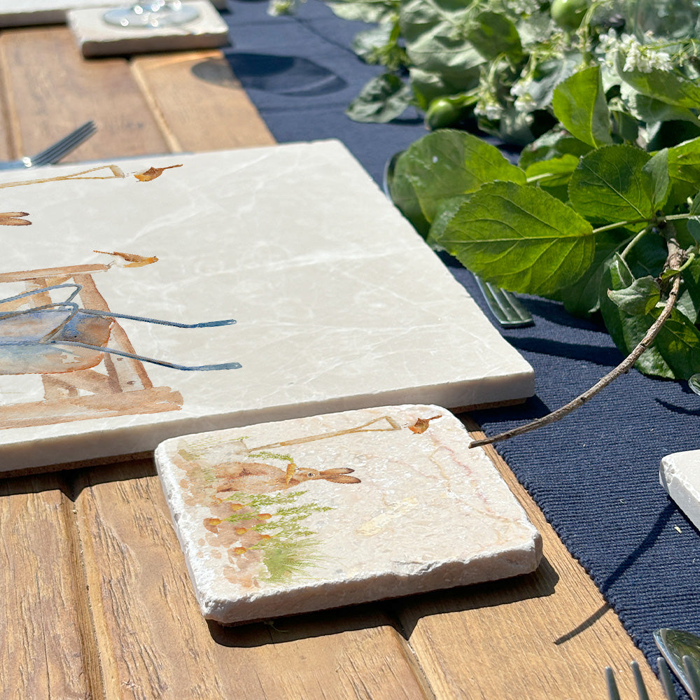 An outdoor table set for a dinner party with marble placemats and coasters, each featuring a watercolour design of a vegetable patch.