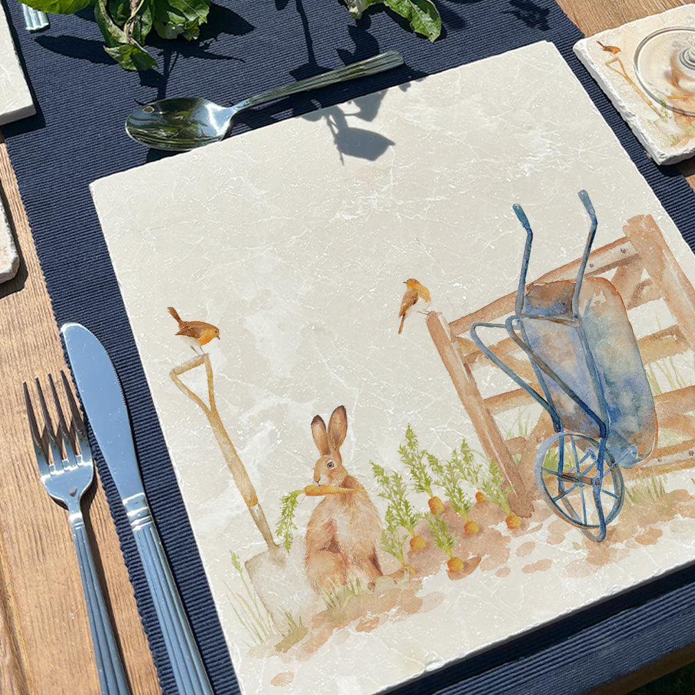 A garden table set with square cream marble placemats featuring a watercolour vegetable patch design. 