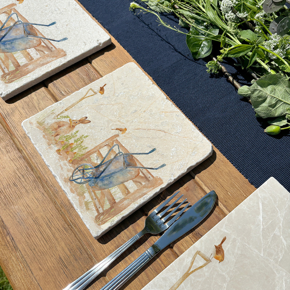 A garden table set with a medium square marble platter that features a watercolour vegetable patch design. The platter is set next to a marble placemat and coaster in the same design.