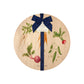 Round beech wood chopping board featuring a watercolour pattern of beetroot, carrots, parsnips, runner beans and radishes. The wooden board is finished with a blue gift ribbon and tag.