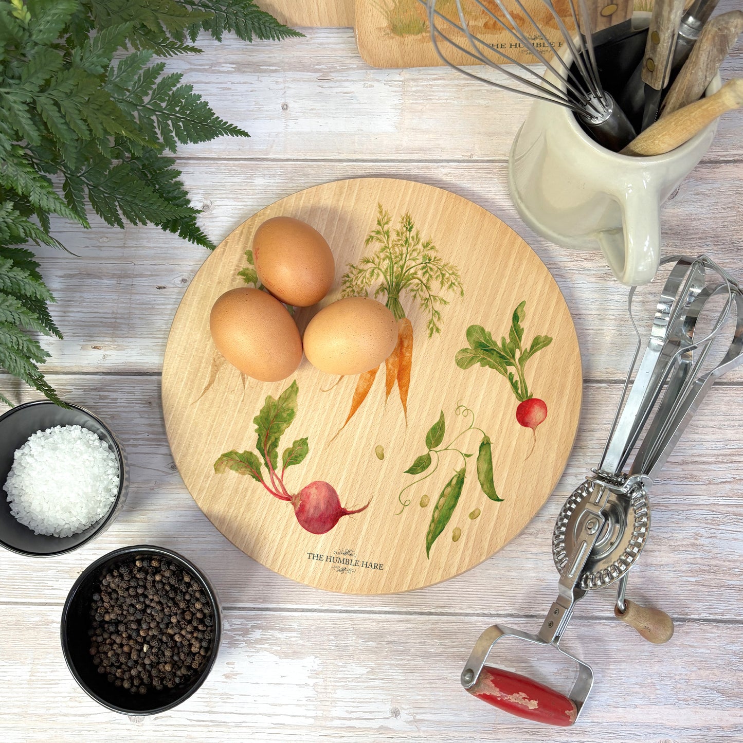 Round wooden chopping board on a kitchen worktop. The beech wood board features a watercolour pattern of beetroot, carrots, parsnips, runner beans and radishes.