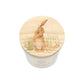 A white glass candle jar with a light wood lid with an illustration of a brown hare washing its ear in long grass.