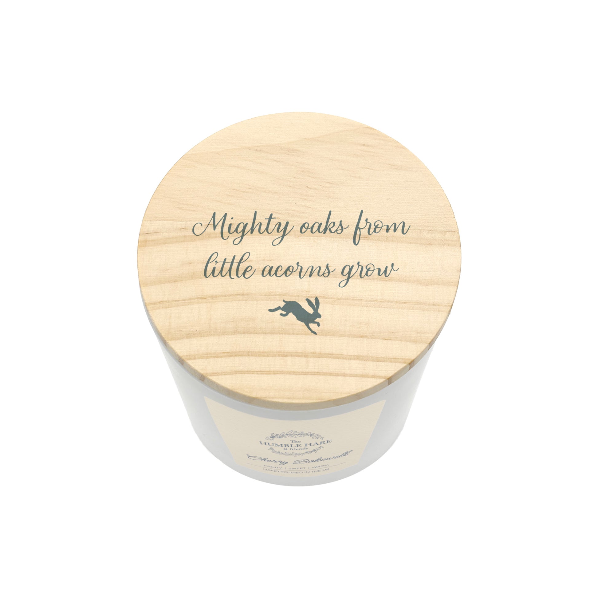 A white glass candle jar with a light wood lid with the quote 'Mighty oaks from little acorns grow' and a small leaping hare silhouette.