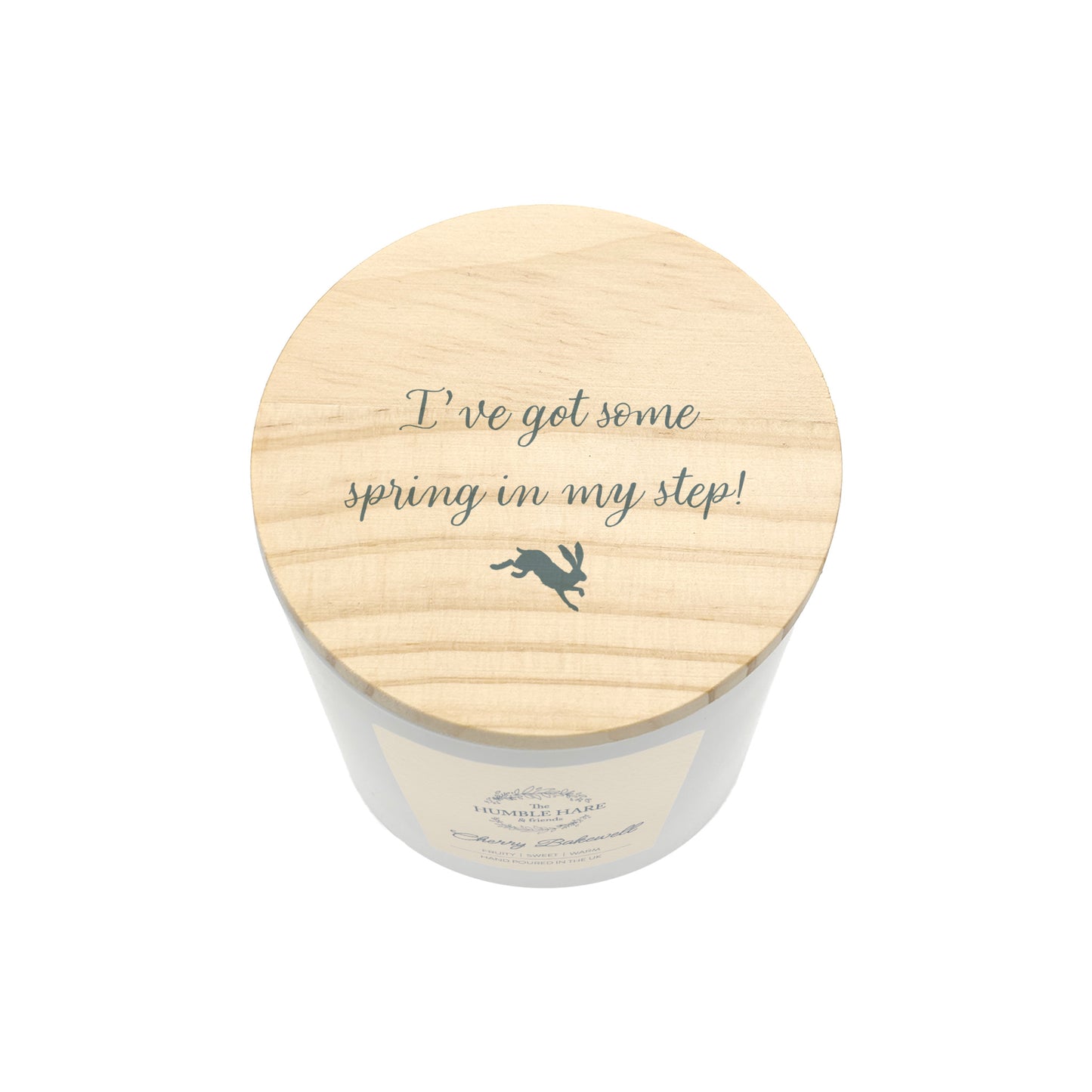A white glass jar candle with a light natural wood lid featuring the phrase 'I've got some spring in my step!' and a small hare silhouette, shown on a white background.