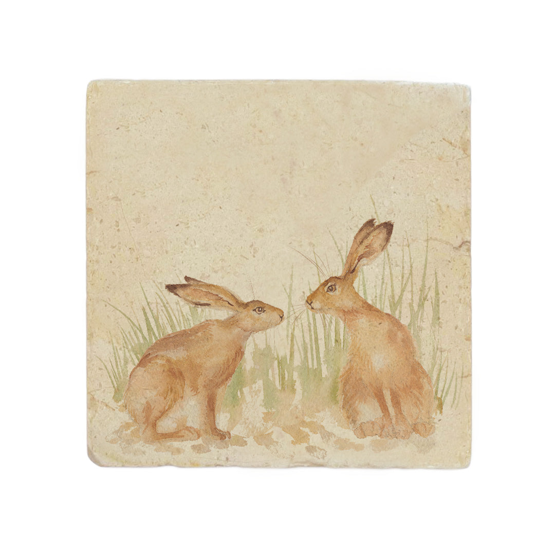 A square cream marble placemat featuring a watercolour countryside animal design of two hares facing each other about to touch noses.